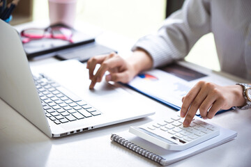 business woman or accountant who are using a calculator to calculate business data Accounting documents and laptop computer at the office business idea