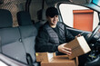 © Artem Varnitsin - Smiling courier sitting on a driver's seat checking delivery information on mobile phone while holding box