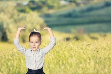 Canvas Print - Happy little girl in raised her hands up in a field of daisies