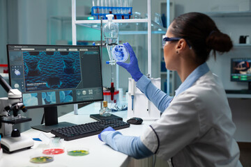 Wall Mural - Biochemist researcher woman holding transparent petri dish analyzing blue solution during microbiology experiment. Scientist doctor working with dna sample in microbiology hospital laboratory