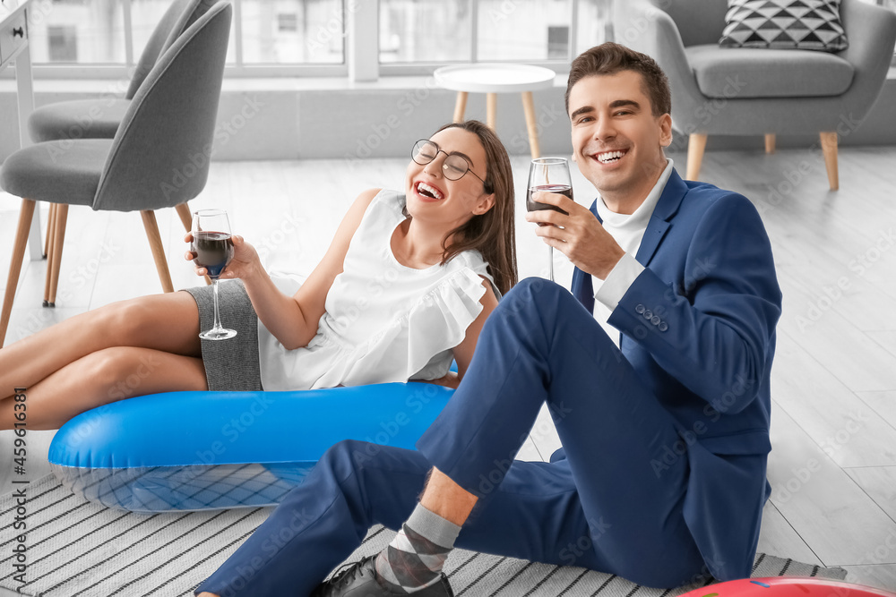 Happy colleagues drinking wine while dreaming about vacation in office