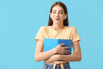 Canvas Print - Young woman with earphones and book on color background