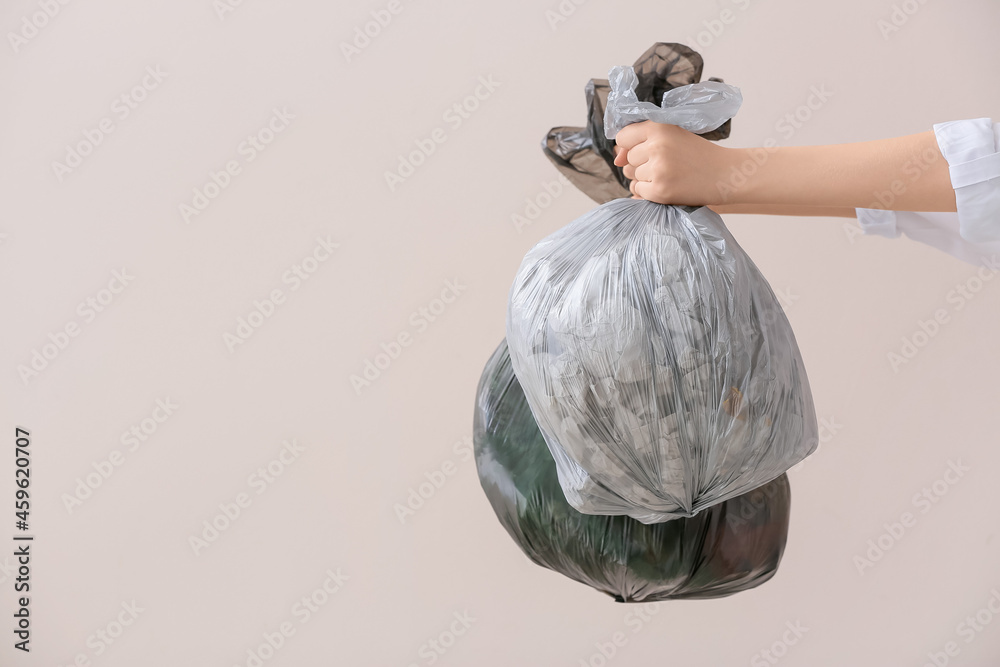 Woman holding bags with garbage on light background