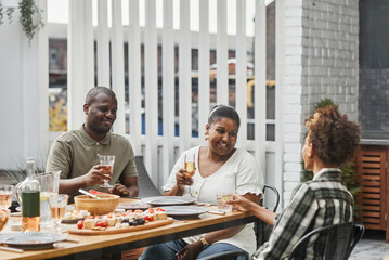 Canvas Print - Portrait of modern African-American family enjoying drinks at dinner together outdoors