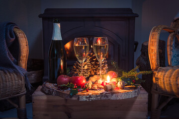 Wall Mural - Christmas or winter holidays concept; home interior with two wicker chairs and rustic table on the wooden box; one bottle and two glasses of champagne, fruits and burning candles