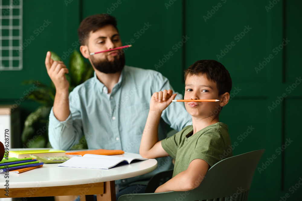 Little boy with his father having fun while doing lessons at home
