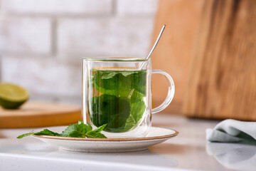 Glass cup of tasty mint tea on table in kitchen, closeup