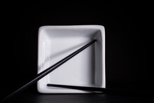 Stainless Steel Chopsticks On White Square Bowl On Black Background.