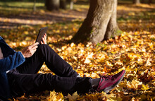 Close Up Of Man Hand With Tablet And His Lifestyle With  In Blue Clothes  In Headphones Listening To Music Outdoors At Park With Autumn Tree Fall Background