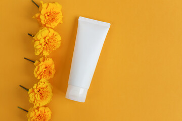 Mockup of white squeeze bottle plastic tube for branding of medicine or cosmetics - cream, gel, skincare. Cosmetic bottle container and marigold flowers on yellow table or background. Top view