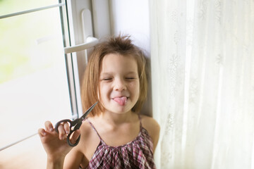 Happy caucasian girl child with scissors cuts off her hair, hooliganism and mischief child, child with a funny oblique haircut, child cut his hair