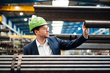 Male Manager Wearing Hardhat Checking Pipe While Working In Factory