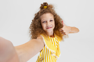 Wall Mural - Front camera view of little smiling curly beautiful girl looking at camera isolated over white studio background.