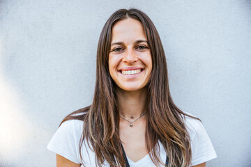 Outdoor portrait of young beautiful woman on grey wall - Millennial looks in camera and smile - Copy space - Concept of expression and naturality