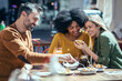 © Westend61 - Happy female friends sharing mobile phone by male friend at restaurant