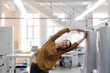 © Westend61 - Smiling businesswoman stretching while exercising in industry