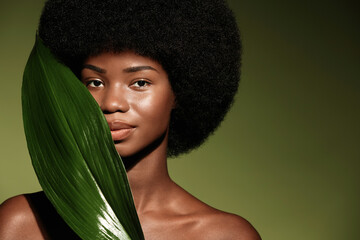 Wall Mural - Natural skin care concept. Beauty portrait of young beautiful african american woman with posing with leaf curly hair against green exotixc plants background.