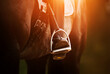 The rider's foot, sitting in the saddle on a horse, is dressed in a black boot and rests on a metal stirrup illuminated by the sun. Equestrian sports. Horse ammunition.