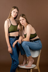 Two pretty teenage girls in tanktops and blue jeans posing for camera in studio