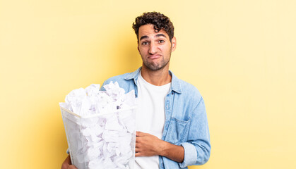 Wall Mural - hispanic handsome man shrugging, feeling confused and uncertain. paper balls trash concept