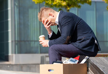 Desperate man sitting outside his former office building; concept of being dismissed