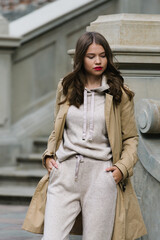 Wall Mural - Portrait of fashionable women in beige sports suit and trench coat posing on the street