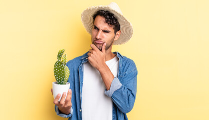 Wall Mural - hispanic handsome man thinking, feeling doubtful and confused farmer and cactus concept