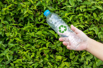 Bottle of fresh water on green tree wall. Hand holding plastic water bottle in concept recycle save the earth and environment