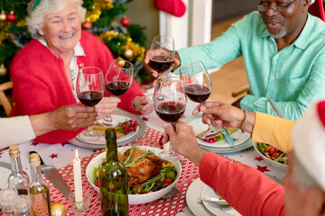 Wall Mural - Diverse group of happy senior friends celebrating christmas with vine together at home