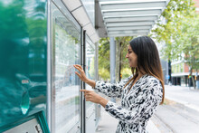 Smiling Female Tourist Watching Map At Bus Stop