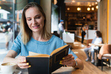 Blond Businesswoman Reading Book At Coffee Shop