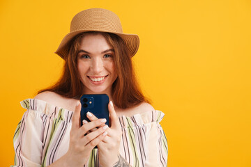 Wall Mural - Young ginger woman in hat smiling and using mobile phone