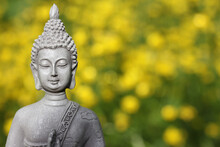 Closeup Shot Of The Buddha Statue In A Garden With Blurred Flower Background