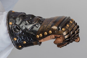 Medieval knightly brown plate gauntlet from Italian armor, in the form of a lion's face and mane, period of the 16th century, on a light background.