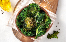 Baked Kale Chips In A Wooden Bowl On A Light Background. Top View. Chips From The Leaves Of Kale Cabbage Close-up. Kale Chips With Olive Oil And Salt, A Tasty Vegan Snack.