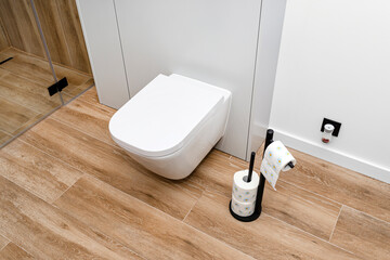 A white ceramic toilet with an closed flap in a modern bathroom, a floor covered with ceramic tiles imitating wood.