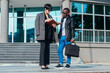© qunica.com - Full-length view of a business caucasian woman holding documents in front of the office building while talking with a black man