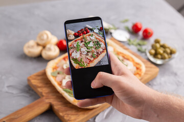 Wall Mural - Chef takes pictures of the cooked of italian pizza with parma ham on smartphone. Photographing food and social networks concept.