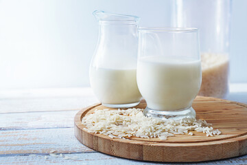 Vegan rice milk, healthy alternative without animal dairy products in a drinking glass and a jug on a wooden kitchen board against a light background, copy space, selected focus