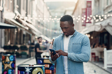 Wall Mural - Young african american man standing on the summer street and using smart phone.