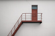 Brown Vintage Wooden Backdoor With Metal Stair And Handrails On White Concrete Building Wall