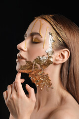 Sticker - Beautiful young woman with  golden paint on her face against black background