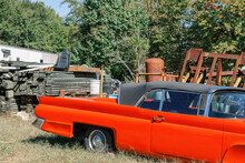 A Retro Vintage Classic Car Parked In An Outdoor Junk Salvage Yard With Piles Of Wood And Metal Scrap Parts.