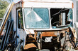 A totaled bus with a shattered windshield and rusty gutted front at a salvage junk yard. 