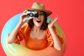 Poster - Surprised woman with photo camera and inflatable ring on color background