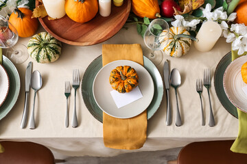 Autumn table setting with fresh pumpkins and flowers in room