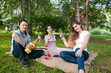 Fototapeta Londyn - Two girls and a man are having a picnic in the summer in the park