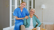 © AboutLife - Smiling young blonde nurse in uniform takes care of senior woman sitting in comfortable armchair in light room