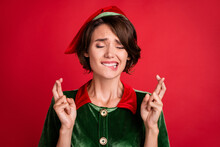 Photo Of Worried Helper Lady Close Eyes Crossed Fingers Bite Lip Wear Elf Costume Hat Isolated Red Color Background