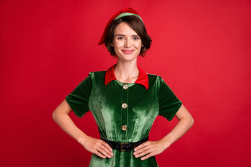 Wall Mural - Photo of confident positive lovely lady hands hips look camera wear elf costume hat isolated red color background